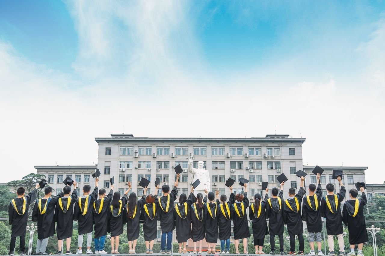 Group of graduates in gowns celebrating outdoors with a building backdrop.