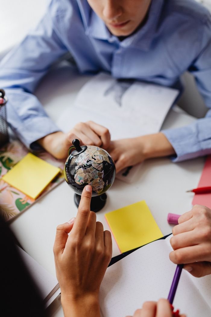 why-choose-us Children studying geography using a globe in a classroom setting.